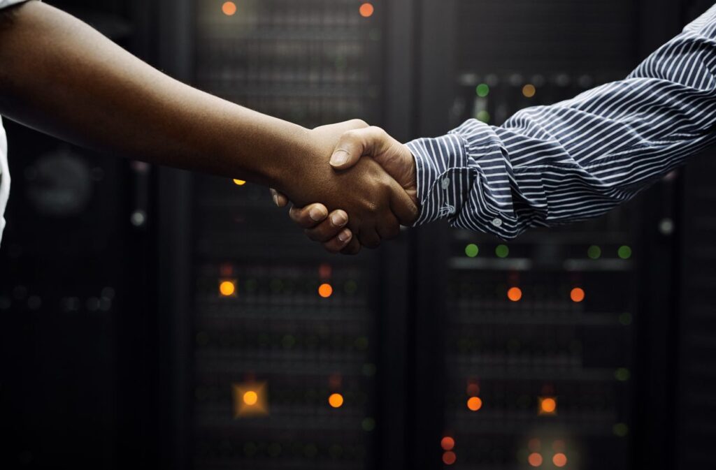 Aperto de mãos em frente a servidores, simbolizando prospecção de clientes para empresas de TI
